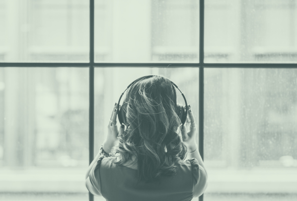 A woman stands at a window with headphones on